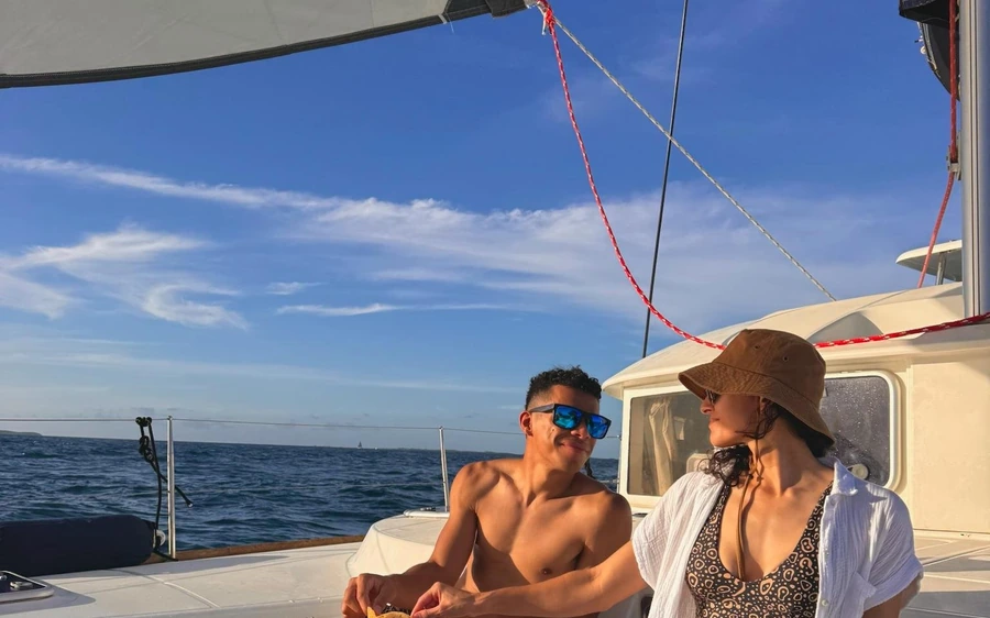 A couple sitting on the deck of a sailing catamaran under the boom