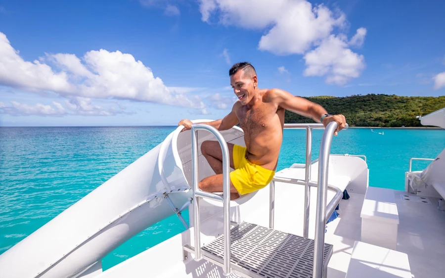 A man sitting on the bow ladder of a boat with a green island behind him