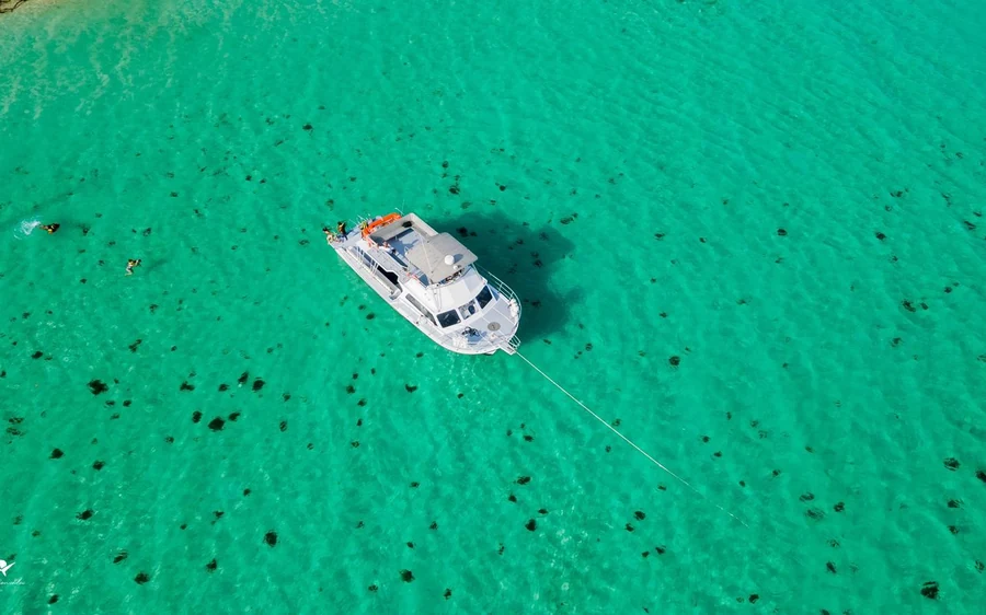 A single white boat alone on bright green shallows with dark coral patches