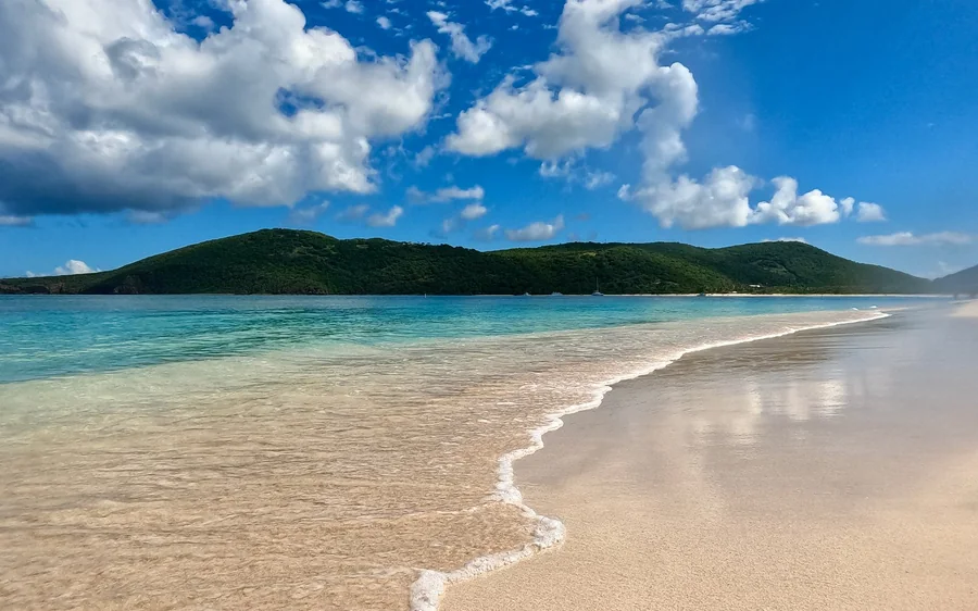 An empty white beach curving away below a green headland