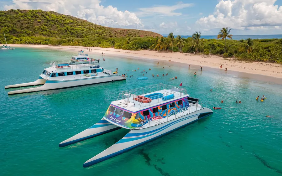 Two party catamarans moored off a palm-backed beach with swimmers between them