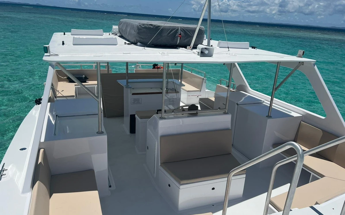The empty shaded deck of a catamaran, with bench seating, a hardtop and a rail