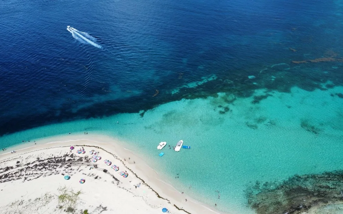 A sandbar and beach from the air, with a boat anchored offshore in turquoise water